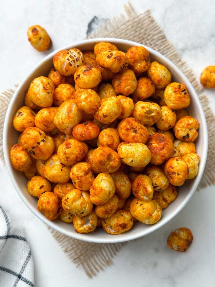 This may contain: a white bowl filled with roasted chickpeas on top of a table next to a napkin