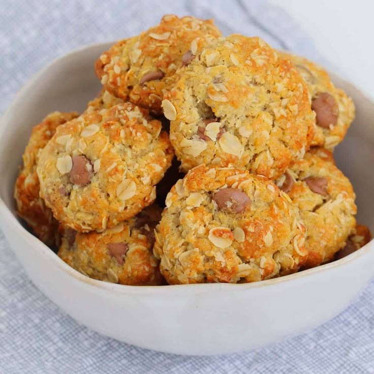 This may contain: a white bowl filled with oatmeal cookies on top of a blue cloth