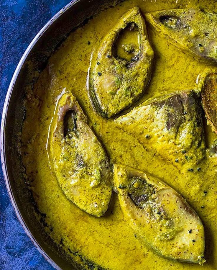 This may contain: a pan filled with fish covered in yellow sauce on top of a blue table cloth