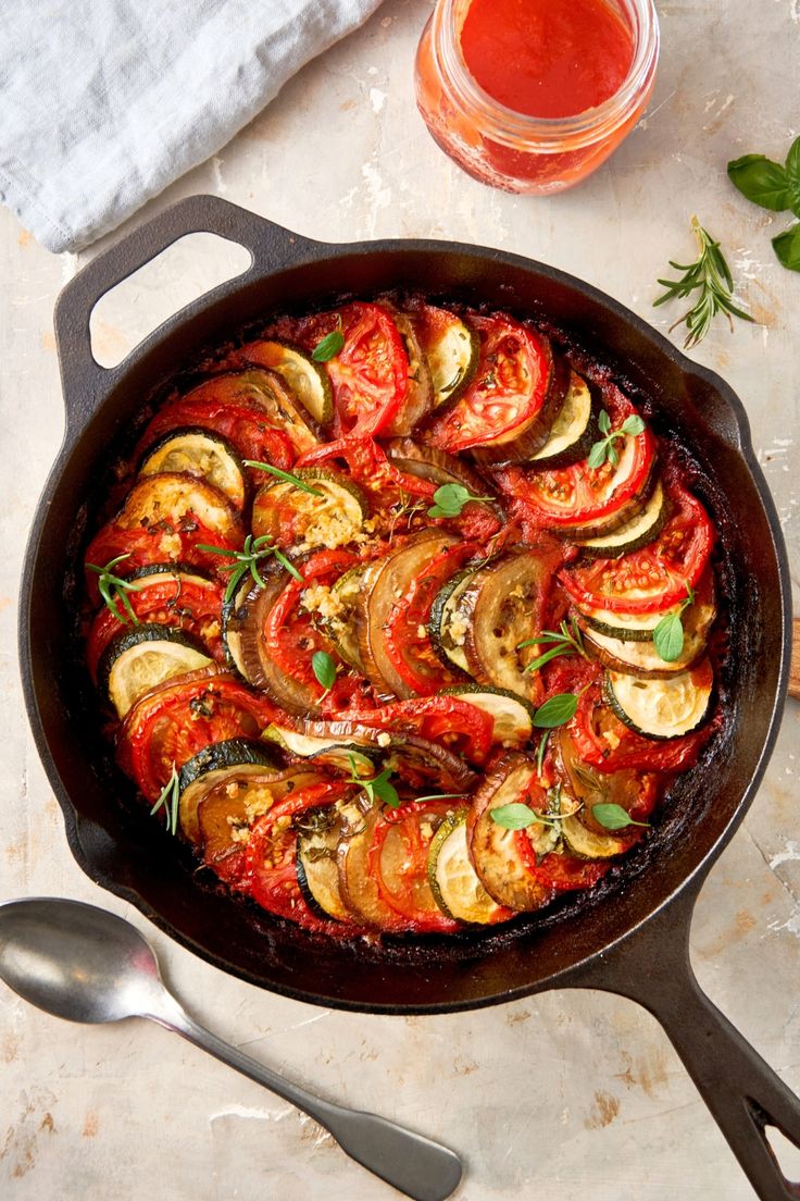 This may contain: an iron skillet with tomatoes and zucchini in it next to a glass of tomato sauce