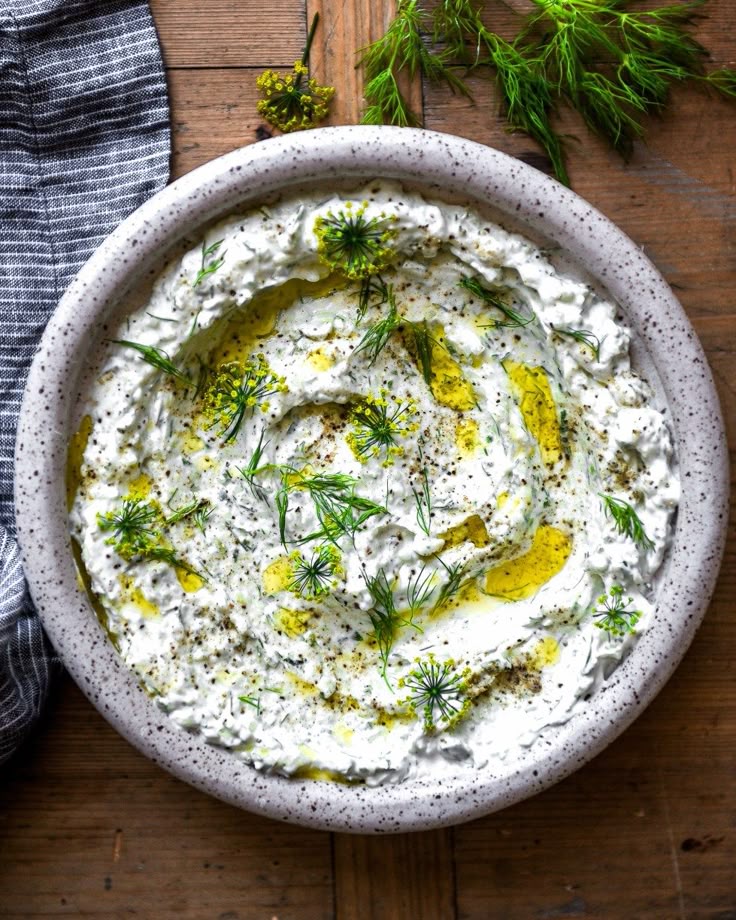 This may contain: a white bowl filled with hummus and dill on top of a wooden table