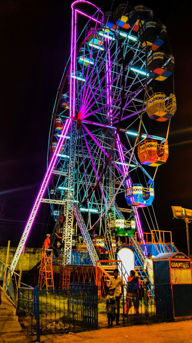This may contain: a ferris wheel lit up at night with people standing around it in the foreground