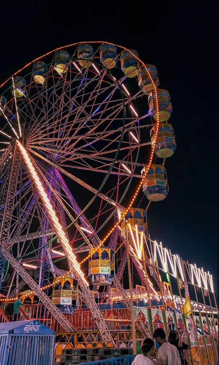 This may contain: the ferris wheel is lit up at night in an amusement park with people standing around it