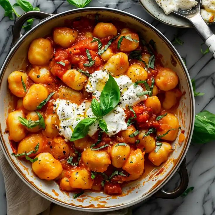 This may contain: a pan filled with gnocchini and tomatoes on top of a marble table