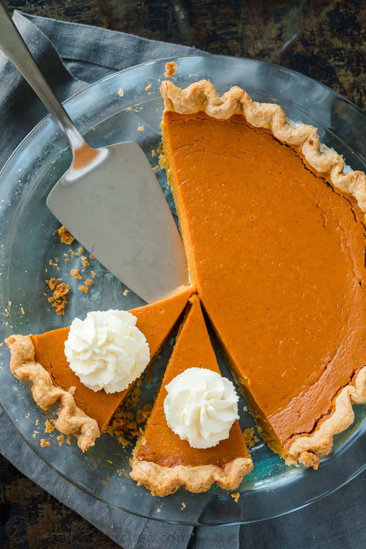 This may contain: a slice of pumpkin pie on a plate with whipped cream and a serving utensil