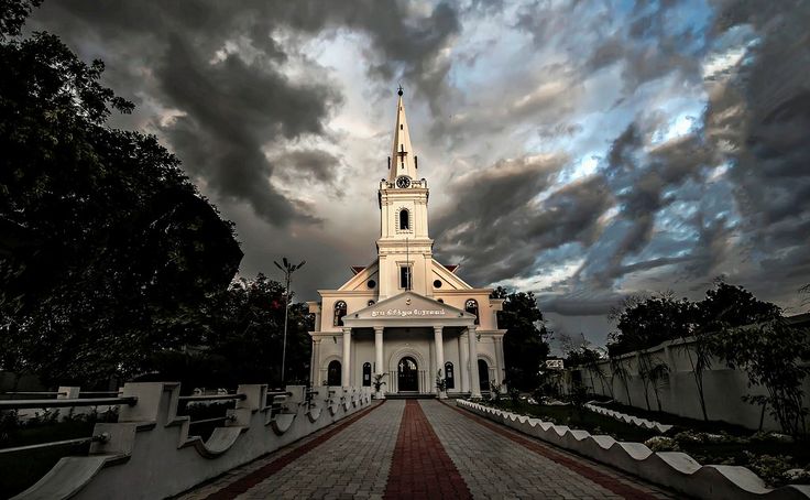This may contain: a large white church with a steeple under a cloudy sky