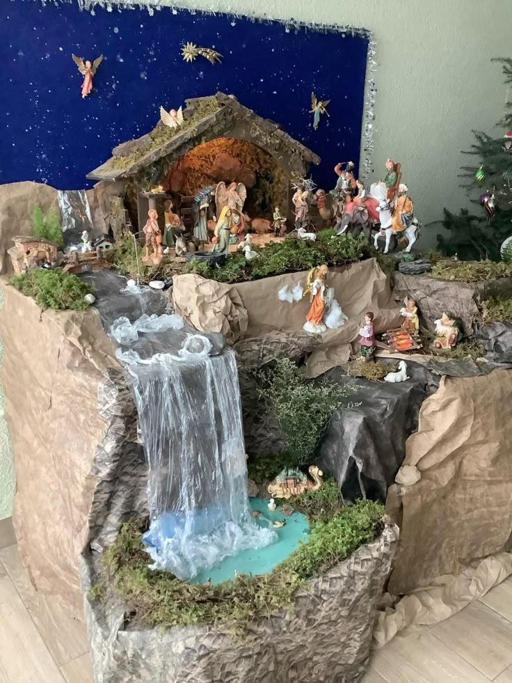 This may contain: a nativity scene is displayed on the wall next to a christmas tree and small waterfall