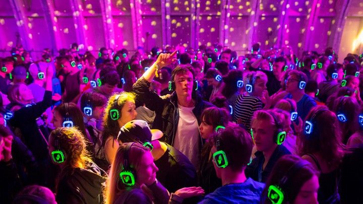 This may contain: a large group of people with headphones on in a room full of purple and green lights