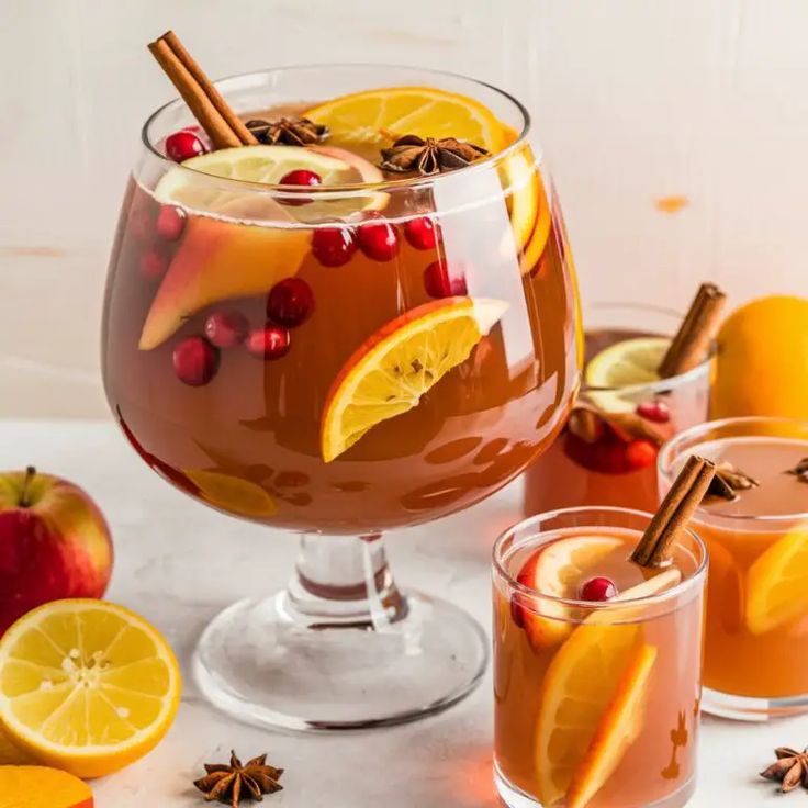 This may contain: two glasses filled with drinks and garnished with orange slices, cinnamons, and pomegranates