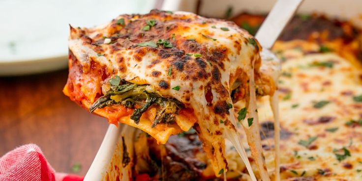 This may contain: a slice of lasagna being lifted from a casserole dish