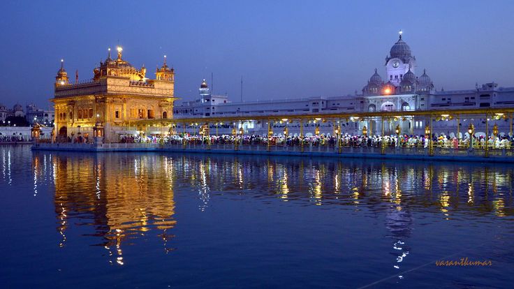 This may contain: the golden temple lit up at night with lights reflecting in the water and people walking around