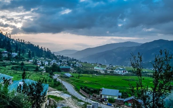 This may contain: a small village on the side of a mountain with green fields and mountains in the background