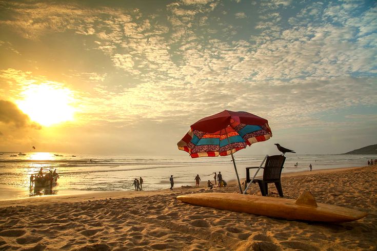 This may contain: an umbrella and chair on the beach with people in the water behind it at sunset