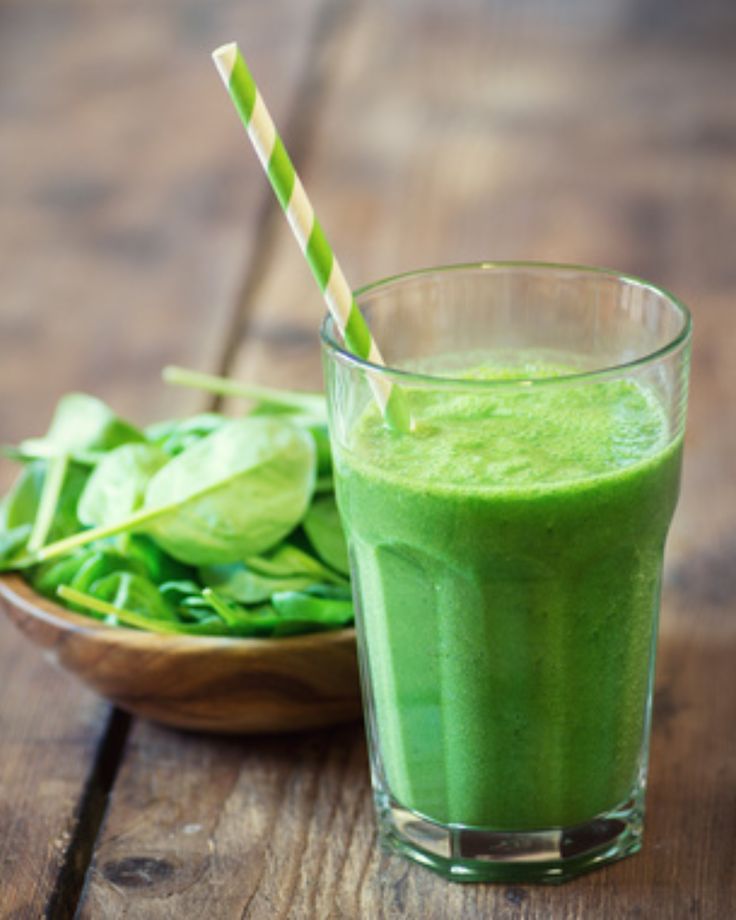 This may contain: a green smoothie in a glass with a straw next to it on a wooden table