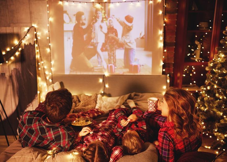 This may contain: two children are laying on a couch in front of christmas lights and a projector screen