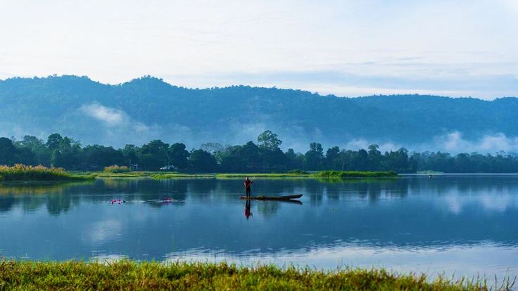 This may contain: a person standing on a boat in the middle of a lake with mountains in the background