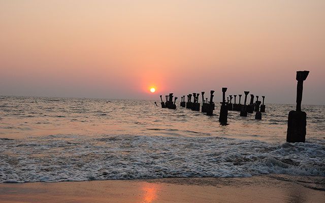 This may contain: the sun is setting over the ocean with old wooden posts sticking out of the water