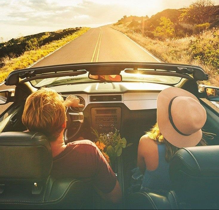 This may contain: two people sitting in the driver's seat of a car driving down a country road