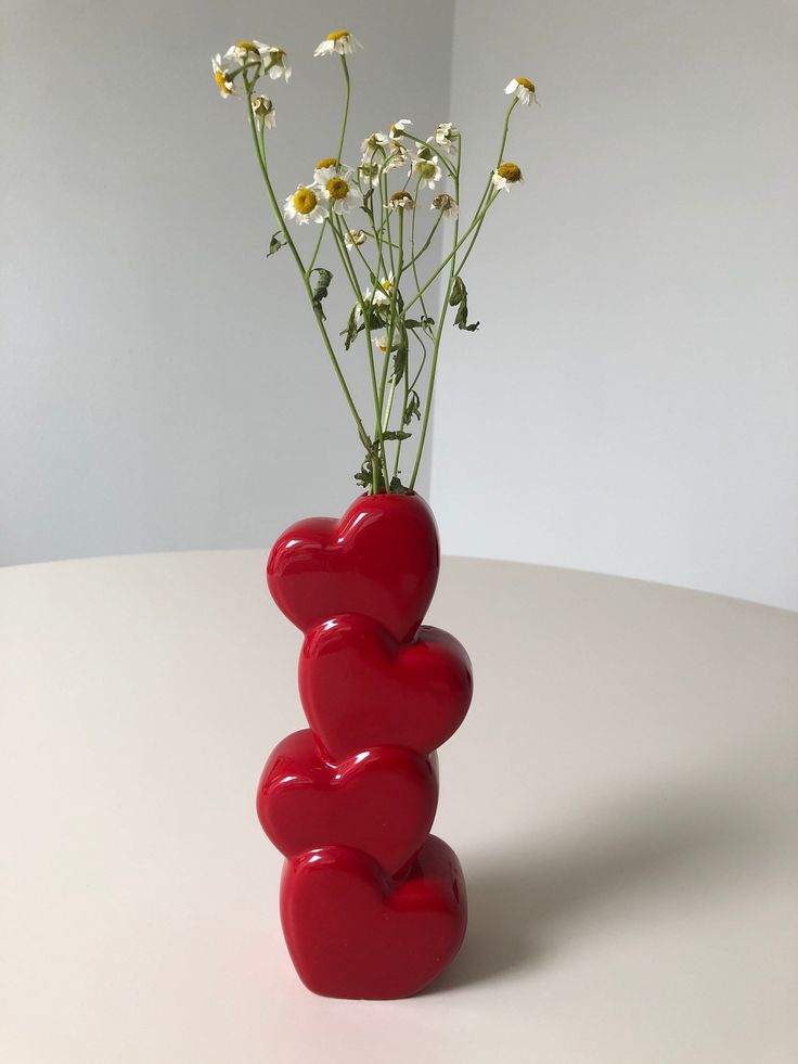 This may contain: two hearts shaped vases with daisies in them on a white table top against a gray wall