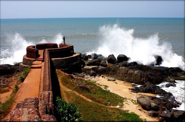 This may contain: a man standing on top of a rock covered beach next to the ocean with crashing waves