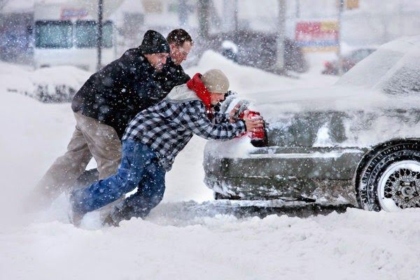This may contain: two men pushing a car out of the snow