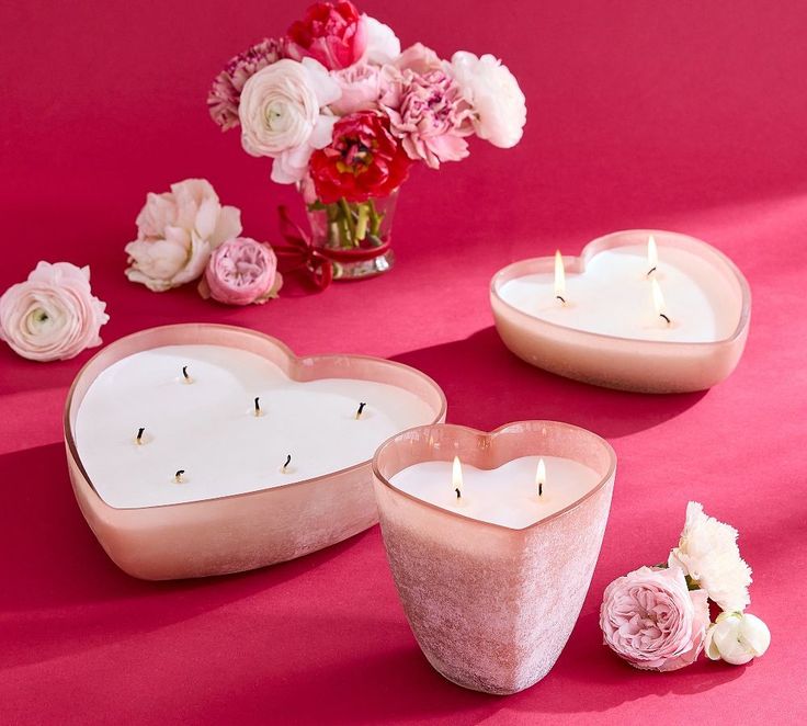 This may contain: two heart shaped candles sitting next to each other on a pink surface with flowers in the background