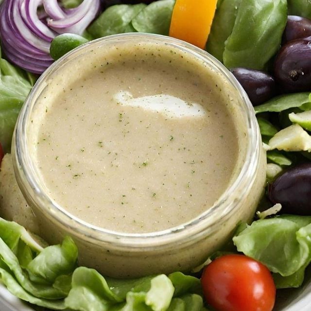 This may contain: a white bowl filled with lettuce, tomatoes and olives next to a salad