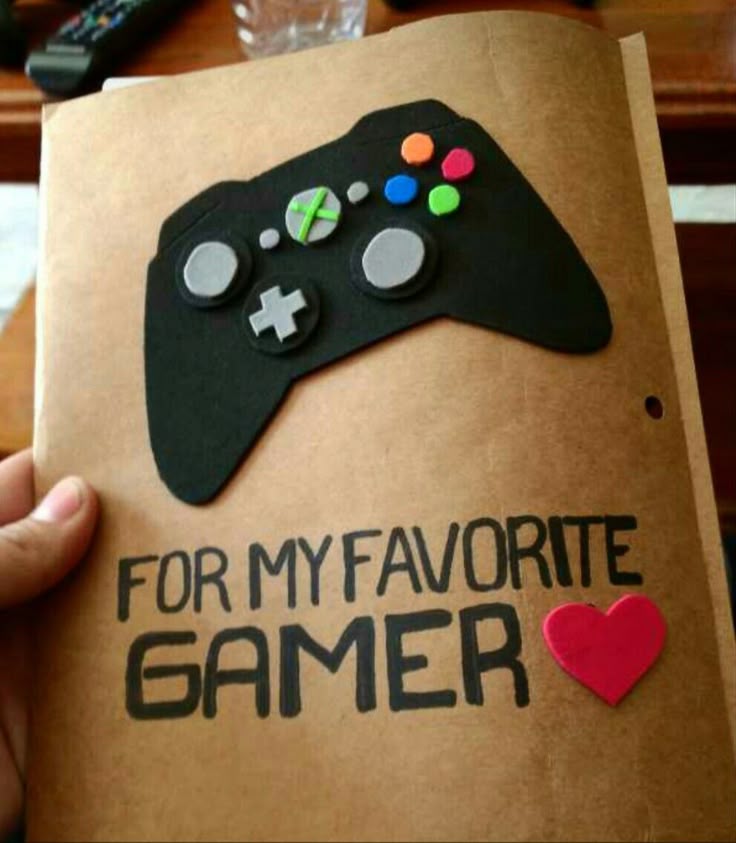 This may contain: someone is holding up a book that has a video game controller on it and the words for my favorite gamer written in black
