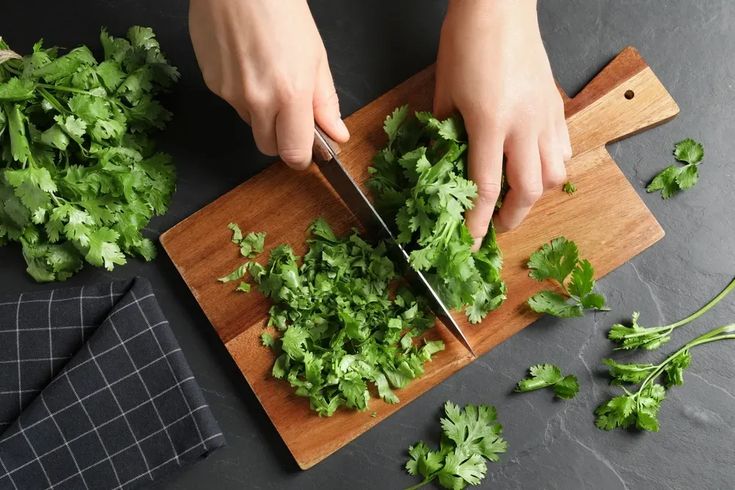 This may contain: a person cutting up some cilantro on top of a wooden cutting board with a knife