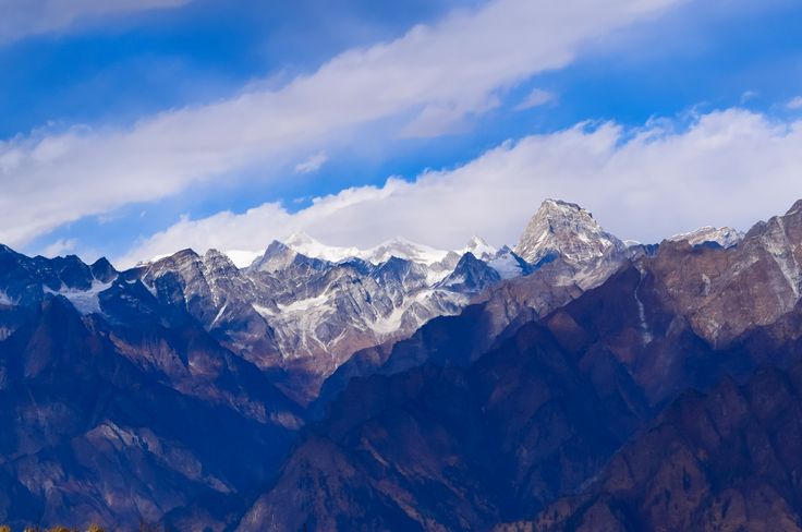 This may contain: the mountains are covered in snow and brown grass, under a blue sky with white clouds