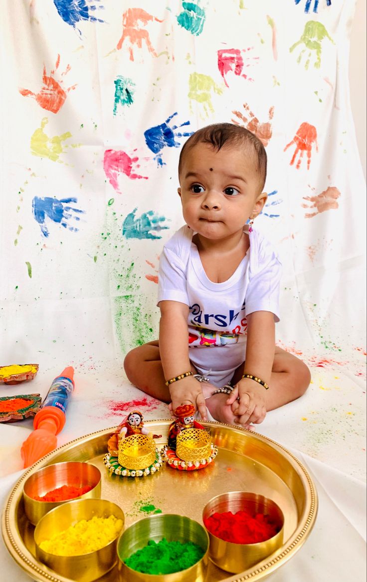 This may contain: a baby sitting on the floor in front of some colorful paints