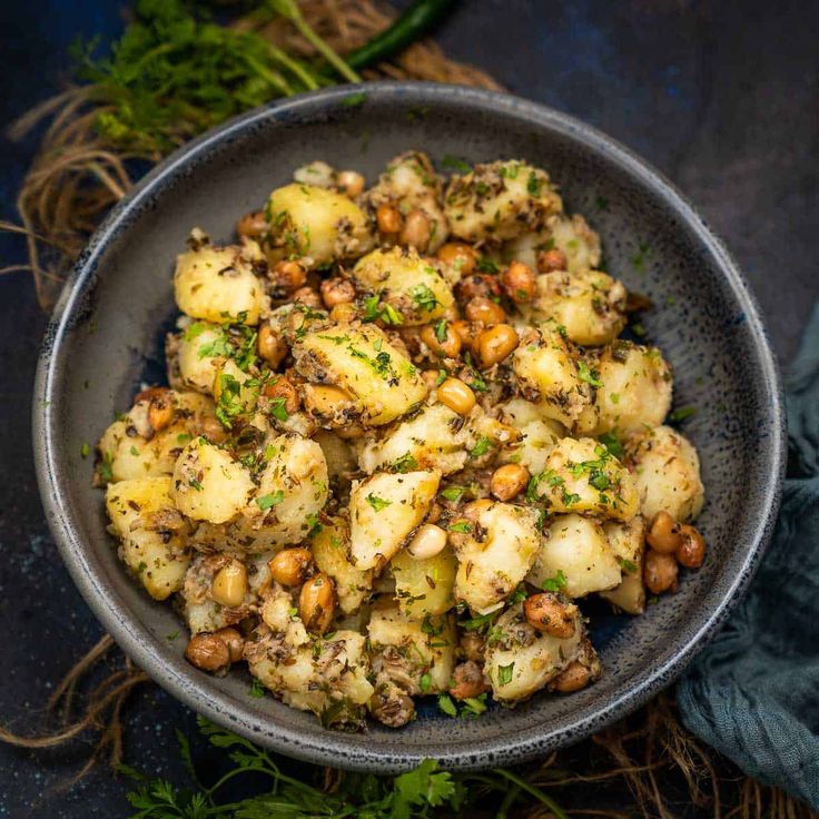 This may contain: a bowl filled with potatoes and nuts on top of a blue cloth next to some parsley