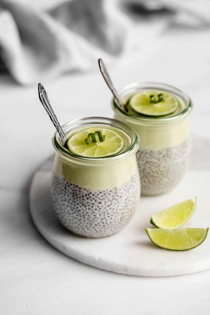 This may contain: two glasses filled with chia pudding and topped with limes on a white plate