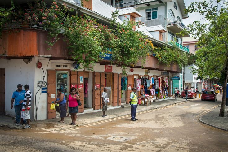 This may contain: some people are standing on the side walk in front of shops and buildings with green trees