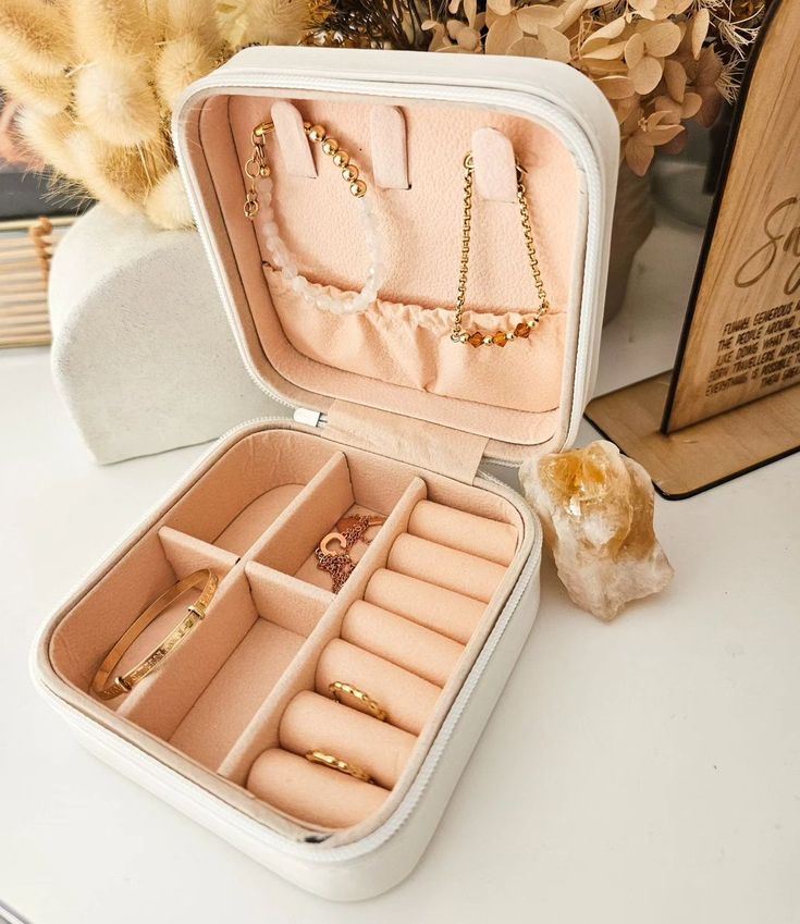 This may contain: an open white box with jewelry inside sitting on a table next to flowers and other items