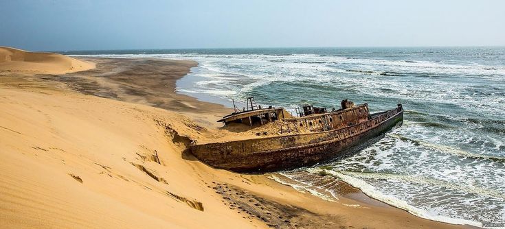 This may contain: an old boat sitting on top of a sandy beach near the ocean's edge