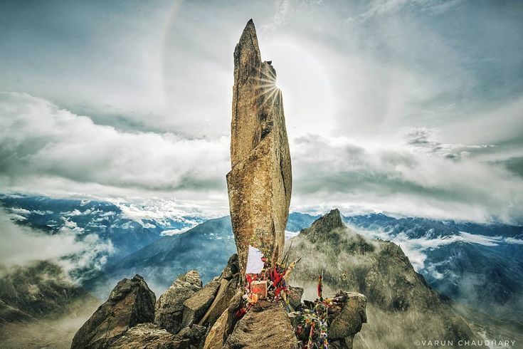 This may contain: a group of people standing on top of a mountain next to a tall rock with a rainbow in the sky