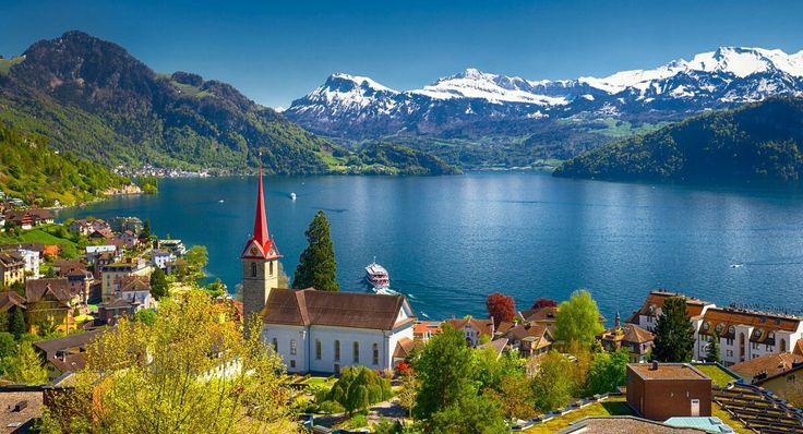 This may contain: a small church on the side of a lake with mountains in the background