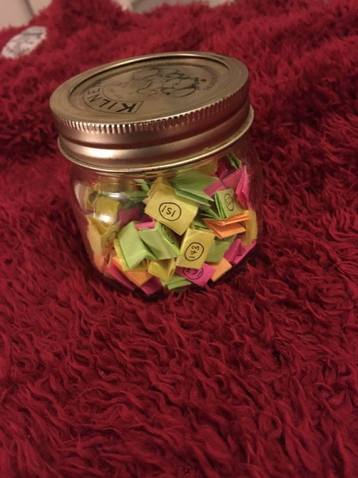 This may contain: a jar filled with lots of colorful origami on top of a red blanket