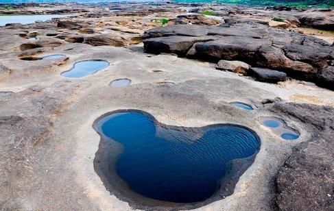 This may contain: there is a heart shaped hole in the rocks by the water that looks like it's floating