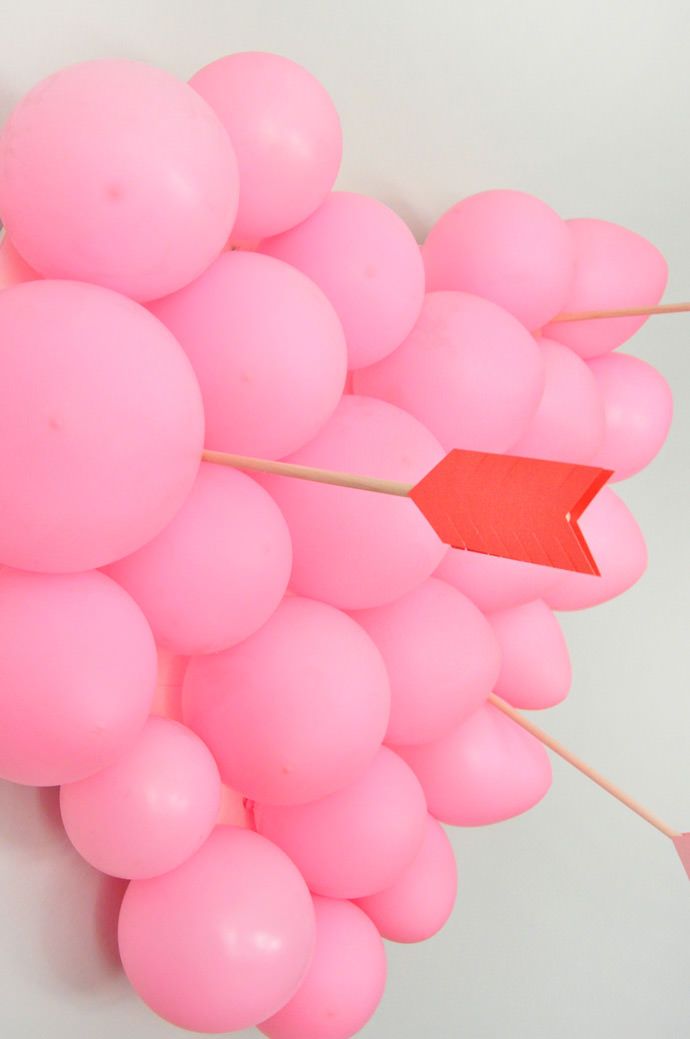 This may contain: a bunch of pink balloons with an arrow sticking out of them on a white wall