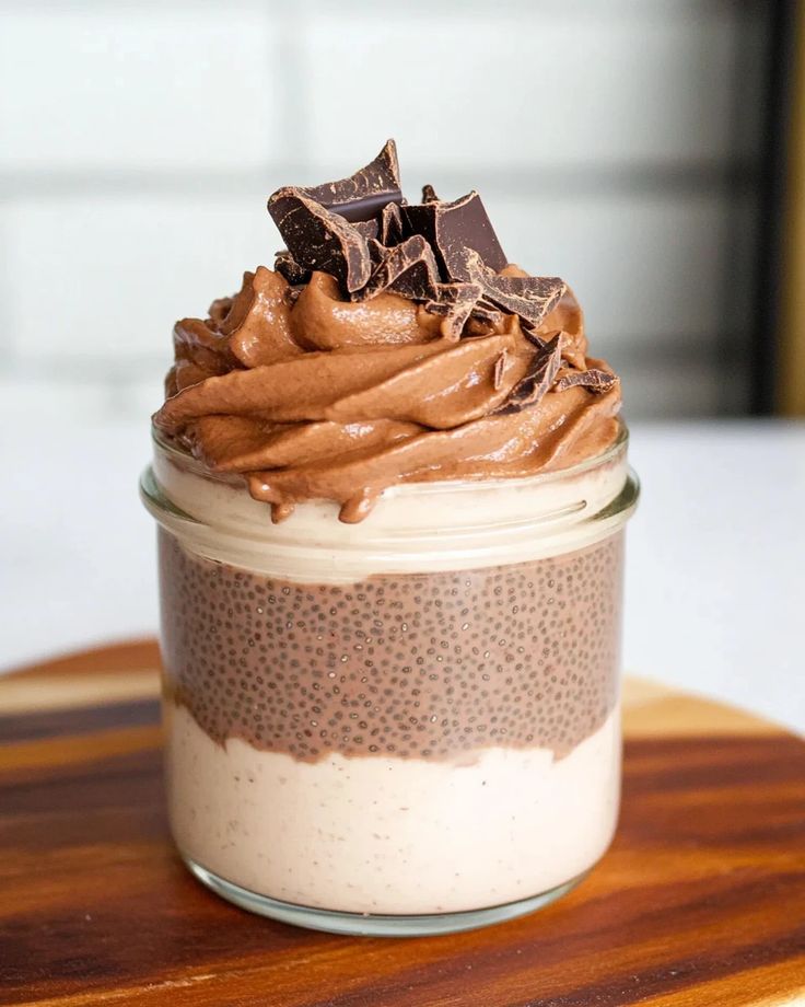 This may contain: a glass jar filled with chocolate frosting on top of a wooden cutting board