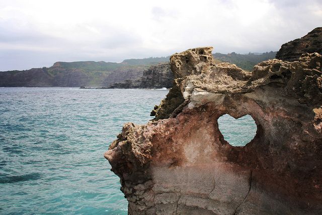 This may contain: a rock formation in the ocean with a heart shaped hole