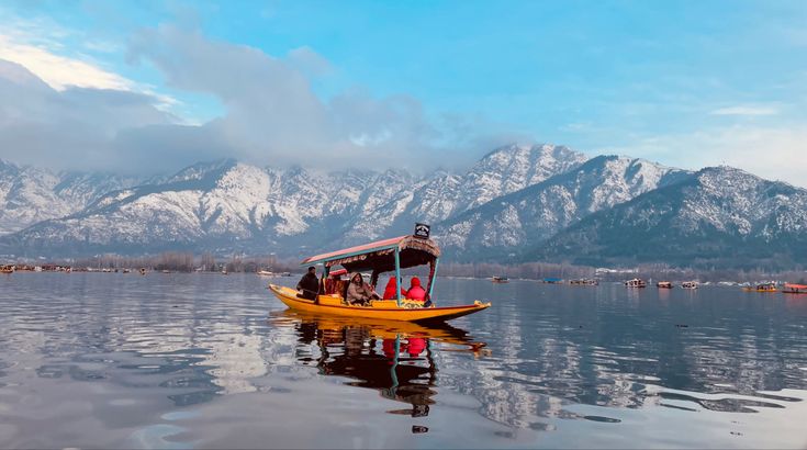 This may contain: a yellow boat floating on top of a lake next to snow covered mountain range in the background