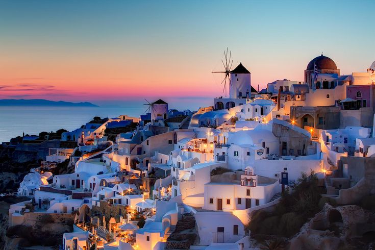 This may contain: the sun is setting over some white buildings and windmills in oia, greece
