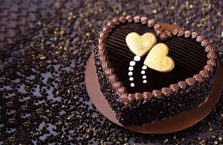This may contain: a heart shaped chocolate cake with two hearts on it's side, surrounded by gold and white sprinkles