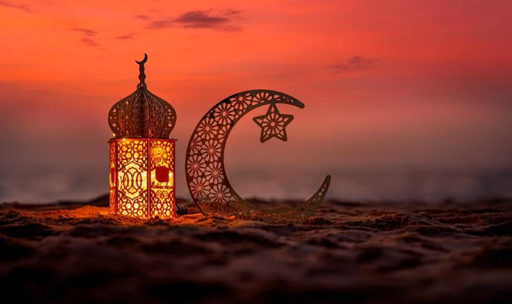 This may contain: an illuminated lantern with a crescent and star on it in front of a red sky