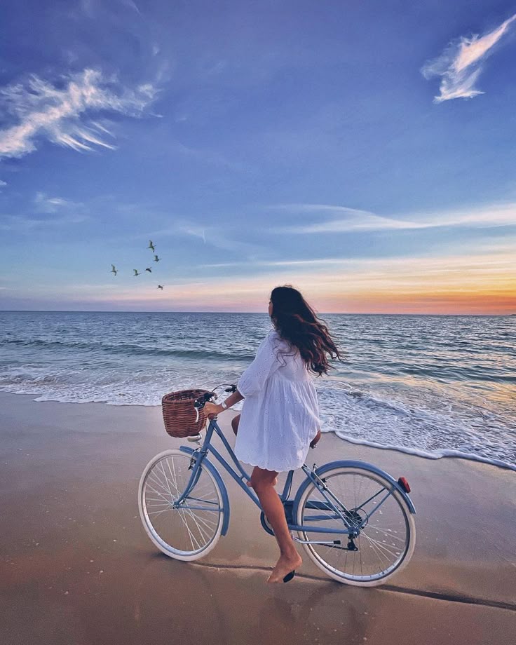 This may contain: a woman riding a bike on top of a beach next to the ocean at sunset