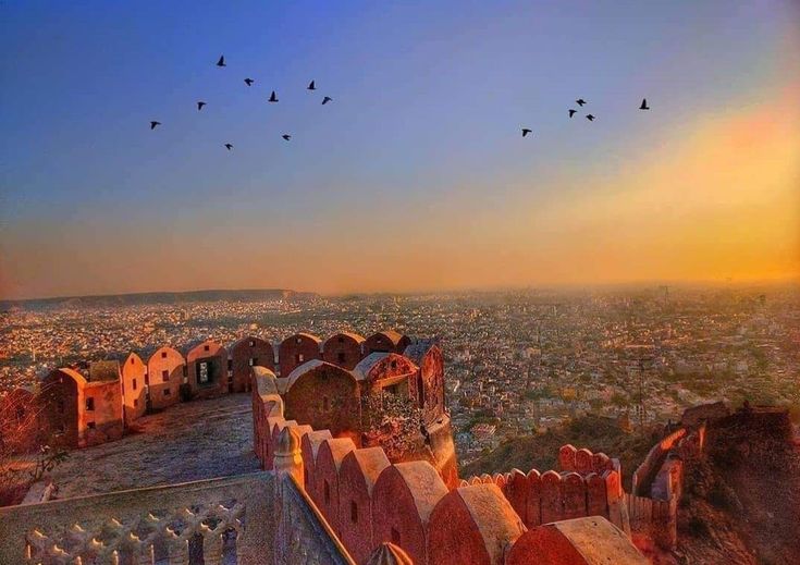 This may contain: birds are flying over the rooftops of an old building at sunset or sunrise time