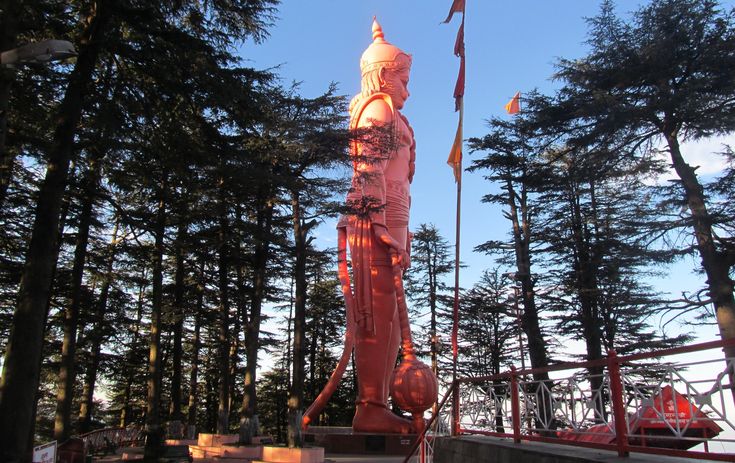 This may contain: there is a large pink statue in the middle of some pine trees with flags flying from it